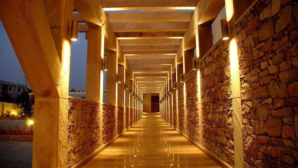 A corridor with stone walls and wooden beams, illuminated by overhead lights. - The Sky Imperial Jaipur (Amer)