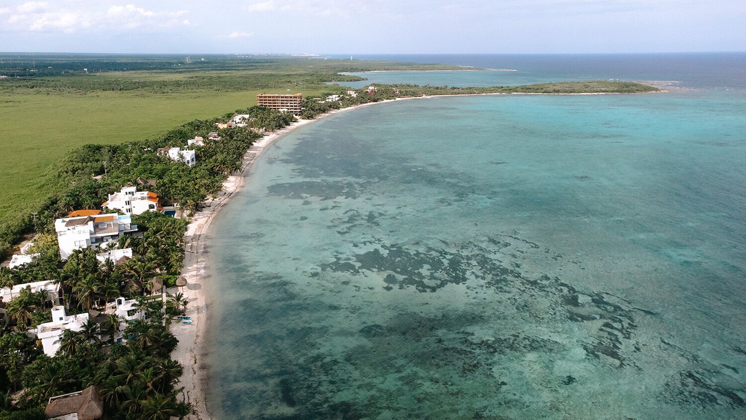 An aerial view of a coastal area with a beach, buildings, and a large body of water.
