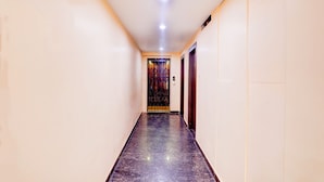 A hallway with a polished marble floor, white walls, and a door with a decorative metal gate at the end. - Deep Ganga inn TripandTrip (Puri)