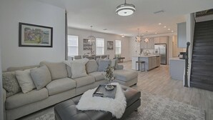 A modern living room with a sofa, ottoman, and a dining area in the background. - Sienna Sunset: Serene Townhome w/ Pool and Lanai (Sarasota)