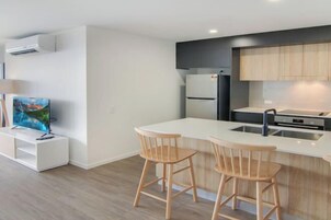 Una cocina moderna con encimera blanca, dos taburetes de madera, horno empotrado y refrigerador.