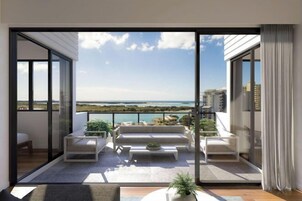 Un balcón moderno con sofá, mesa de centro y plantas en macetas, con vistas a un paisaje costero.