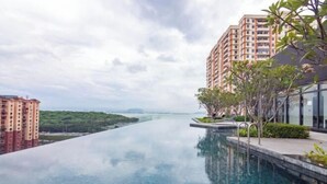 Un hotel moderno con piscina a sfioro sul tetto e vista su una città e aree verdi.