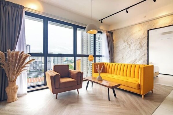 A modern living room with a sofa, armchair, and coffee table, large windows with a city view, and a stone accent wall. - Urban Suites by Stellar ALV (Jelutong)