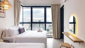 Una moderna camera d'hotel con due letti, una grande finestra vista città e una piccola scrivania con uno specchio.