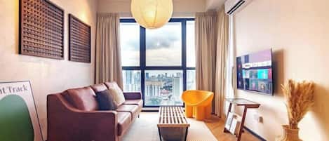A modern living room with a sofa, a coffee table, a TV, and a large window with a city view.