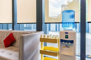 Un distributeur d’eau et un canapé avec un coussin rouge, dans une pièce dotée de grandes fenêtres.