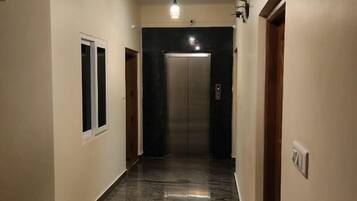 A hallway with a marble floor, a light fixture, and an elevator.