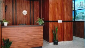 Uma área de recepção com balcão de madeira, um relógio e plantas em vasos.
