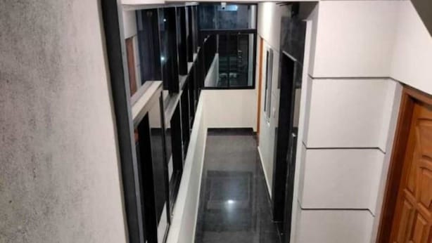 Um corredor moderno com piso preto polido, paredes brancas e uma porta de madeira no final.
