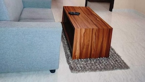 Sala moderna com um sofá cinza, uma mesa de centro de madeira e um espelho refletindo uma cama.