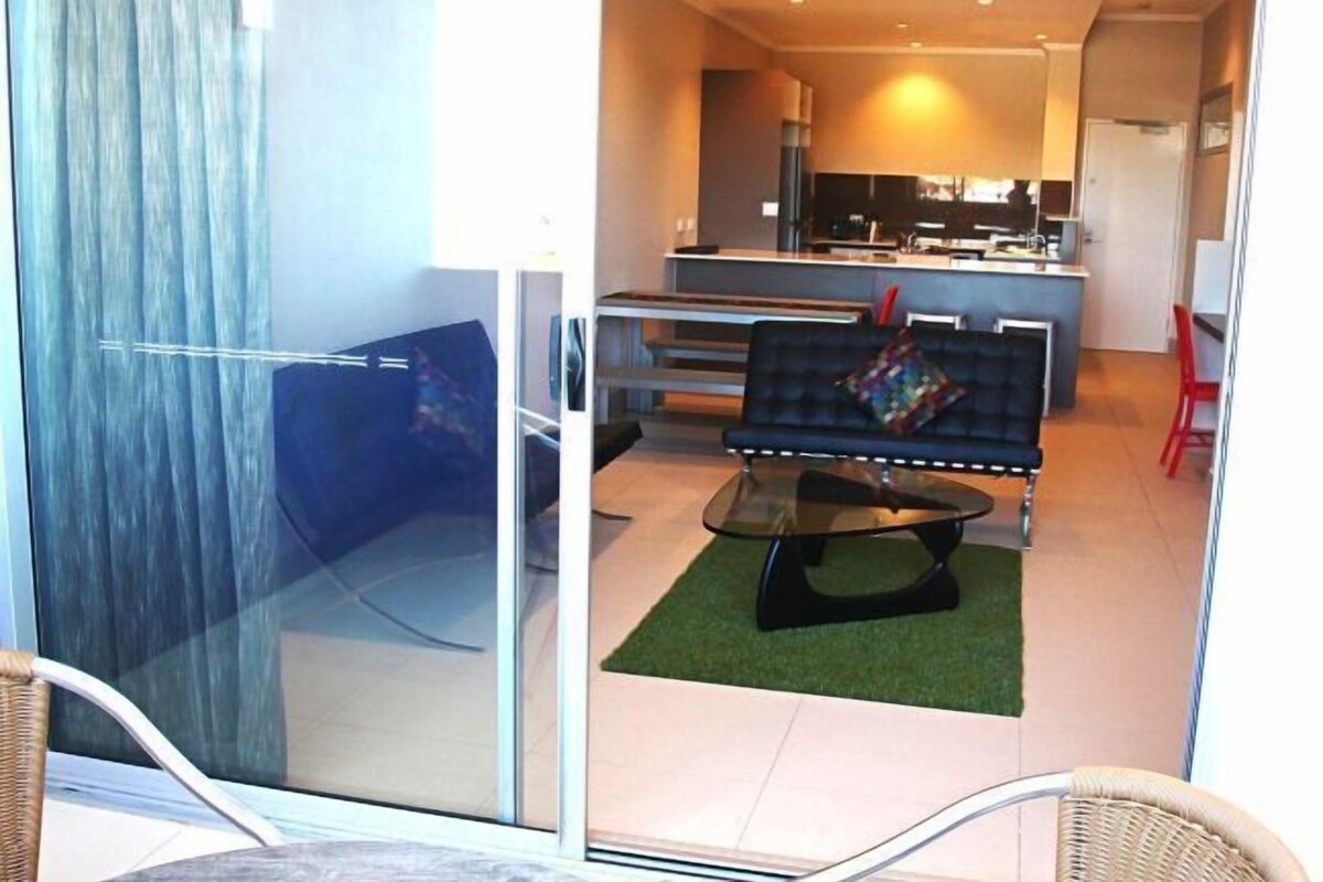A modern living area with a sofa, a glass partition, and a kitchen in the background.