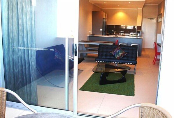 A modern living area with a sofa, a glass partition, and a kitchen in the background. - Laguna Serviced Apartments (Toowoomba)