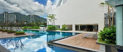 A modern building with a swimming pool, outdoor seating, and a view of mountains.