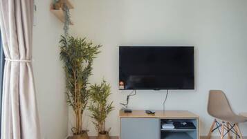 A modern living room with a flat-screen TV mounted on the wall, a wooden cabinet with a built-in shelf, a potted plant, and a chair.