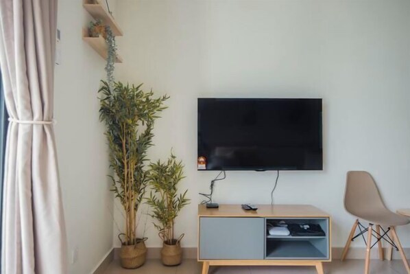 A modern living room with a flat-screen TV mounted on the wall, a wooden cabinet with a built-in shelf, a potted plant, and a chair. - Studio Zen@Midhills Genting Highlands (Free WiFi) (Genting Highlands)