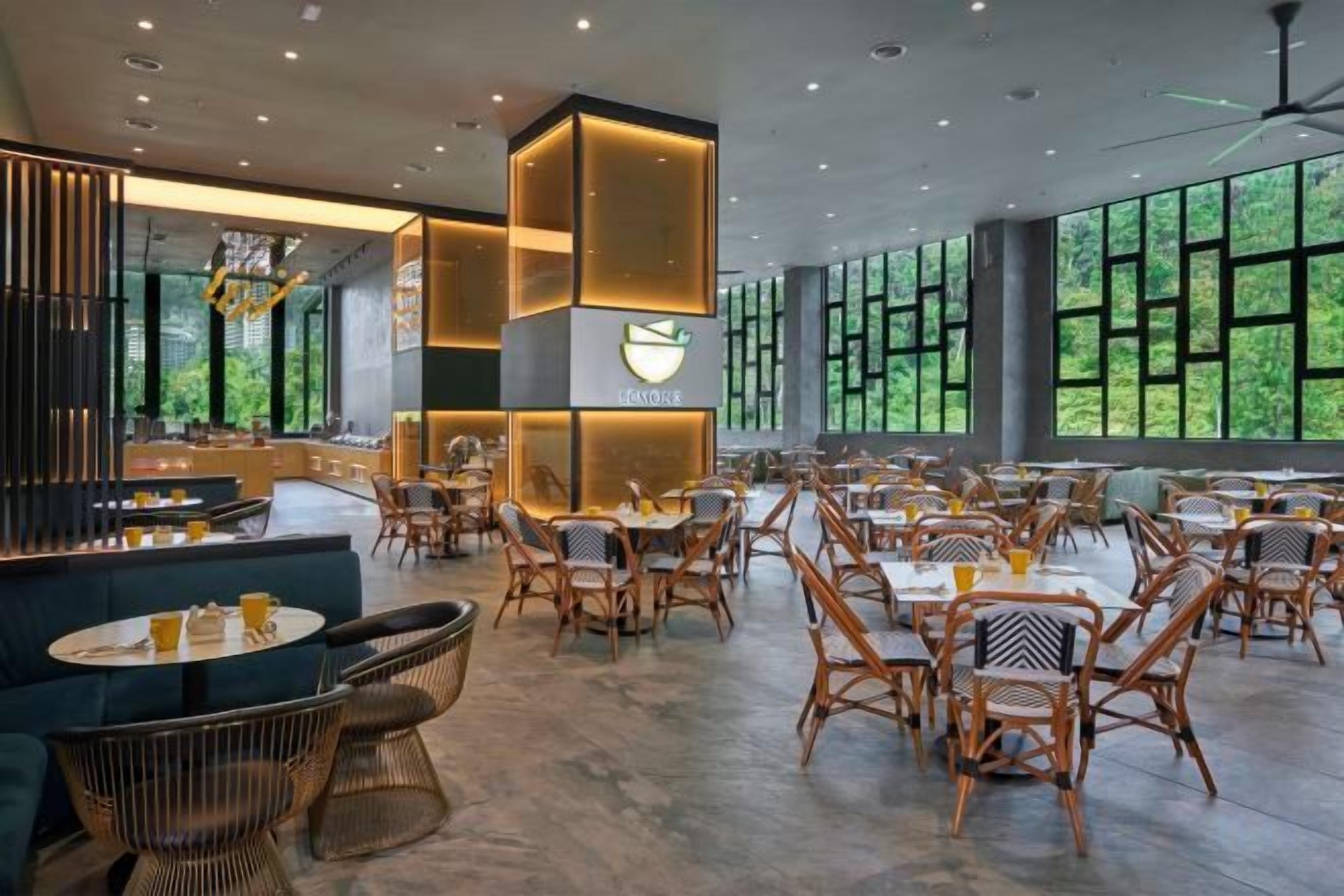 Un restaurante moderno con techos altos, ventanas amplias y diferentes opciones de asientos, incluyendo mesas y sillas.