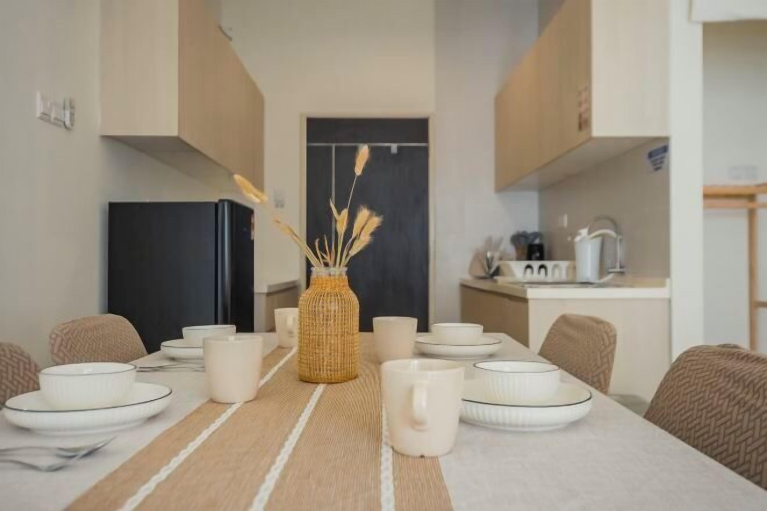 A dining area with a table set for four, a kitchen in the background, and a woven basket centerpiece.
