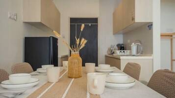 A dining area with a table set for four, a kitchen in the background, and a woven basket centerpiece.