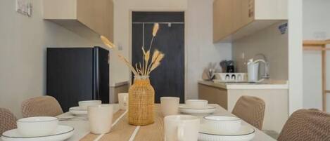 A dining area with a table set for four, a kitchen in the background, and a woven basket centerpiece.
