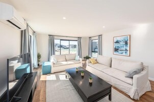 A modern living room with a large flat-screen TV, two sofas, a coffee table, and a large window offering a view of the city.
