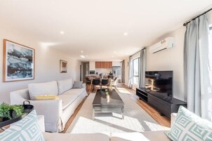 A modern living room with a sofa, coffee table, TV, and kitchen in the background.