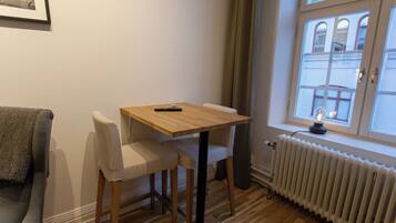 A small room with a wooden table and two chairs, a radiator, and a window with a view of buildings.