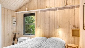 A bedroom with a bed, a window, a shelf with decorative items, and a wall-mounted electrical box.