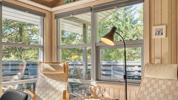 A sunroom with large windows, wooden furniture, and a table with decorative items.