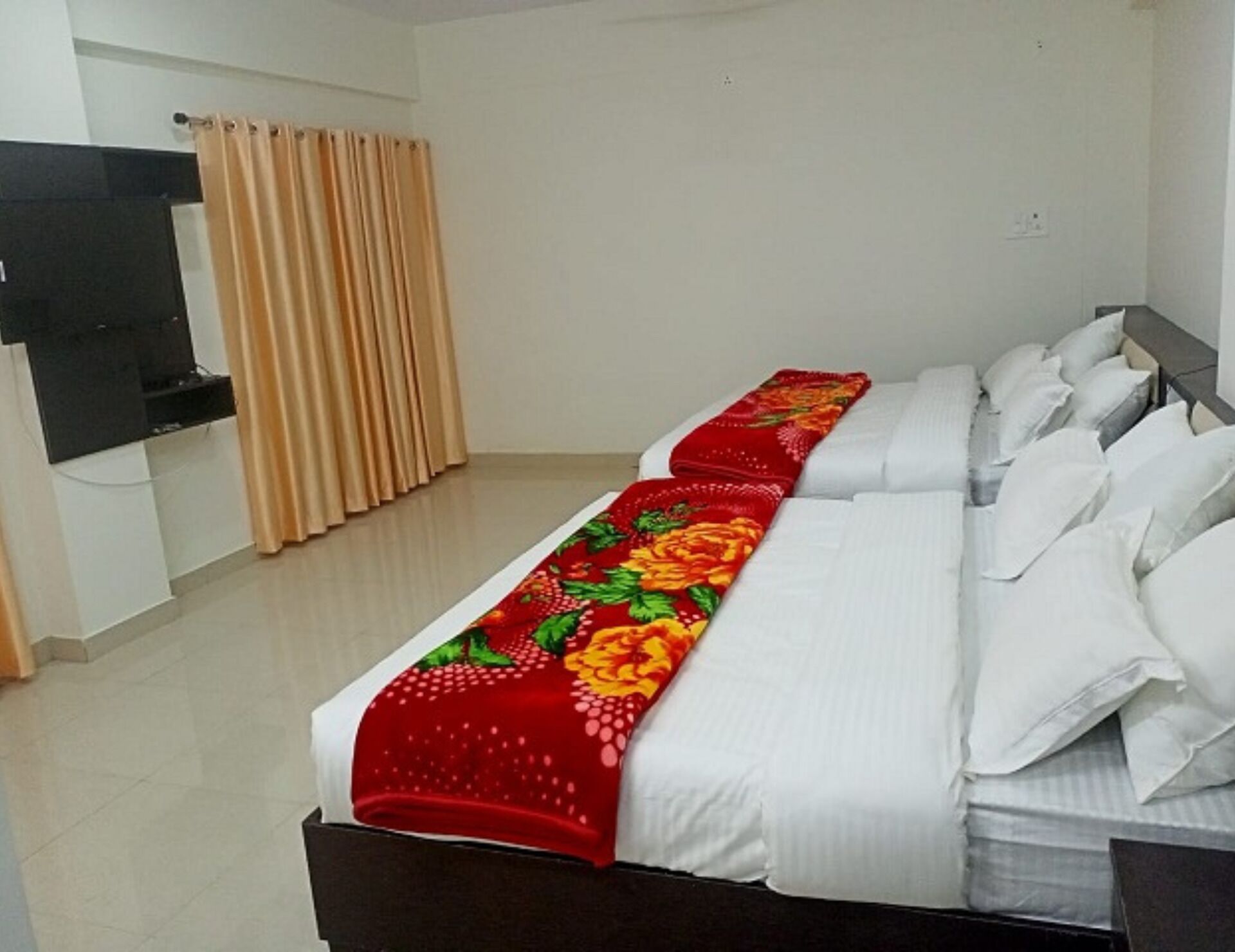 Une chambre d’hôtel avec un grand lit, du linge de lit blanc et une couvre-lit à motifs floraux rouges.