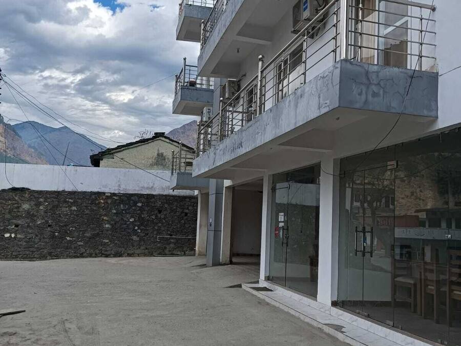 Un immeuble à plusieurs étages doté de balcons, d’un mur en pierre et ayant une chaîne de montagnes en toile de fond.