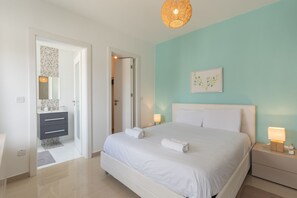 Un dormitorio con cama, mesitas de noche, una puerta que da al baño y un cuadro colgado en la pared.