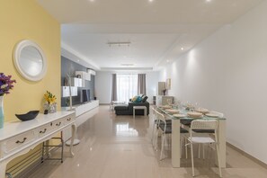 A modern kitchen with white cabinets, a dining area with a glass table, and a living room with a sofa and curtains. - St.Julians apartment (San Gwann)