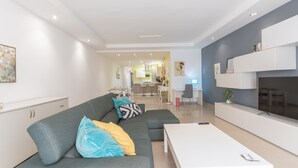 Un soggiorno moderno con un divano grigio, un tavolino da caffè bianco e una TV montata a parete.
