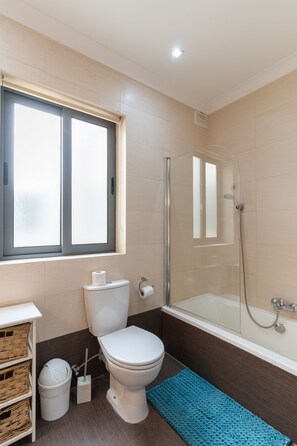 A modern bathroom with a toilet, a glass-enclosed shower, a bathtub, and a window. - St.Julians apartment (San Gwann)