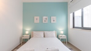 Un letto rifatto con lenzuola bianche e due asciugamani, una parete color verde acqua e tre quadri appesi.