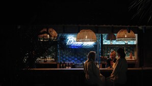 Un bar avec un néon, des lampes suspendues et un comptoir.