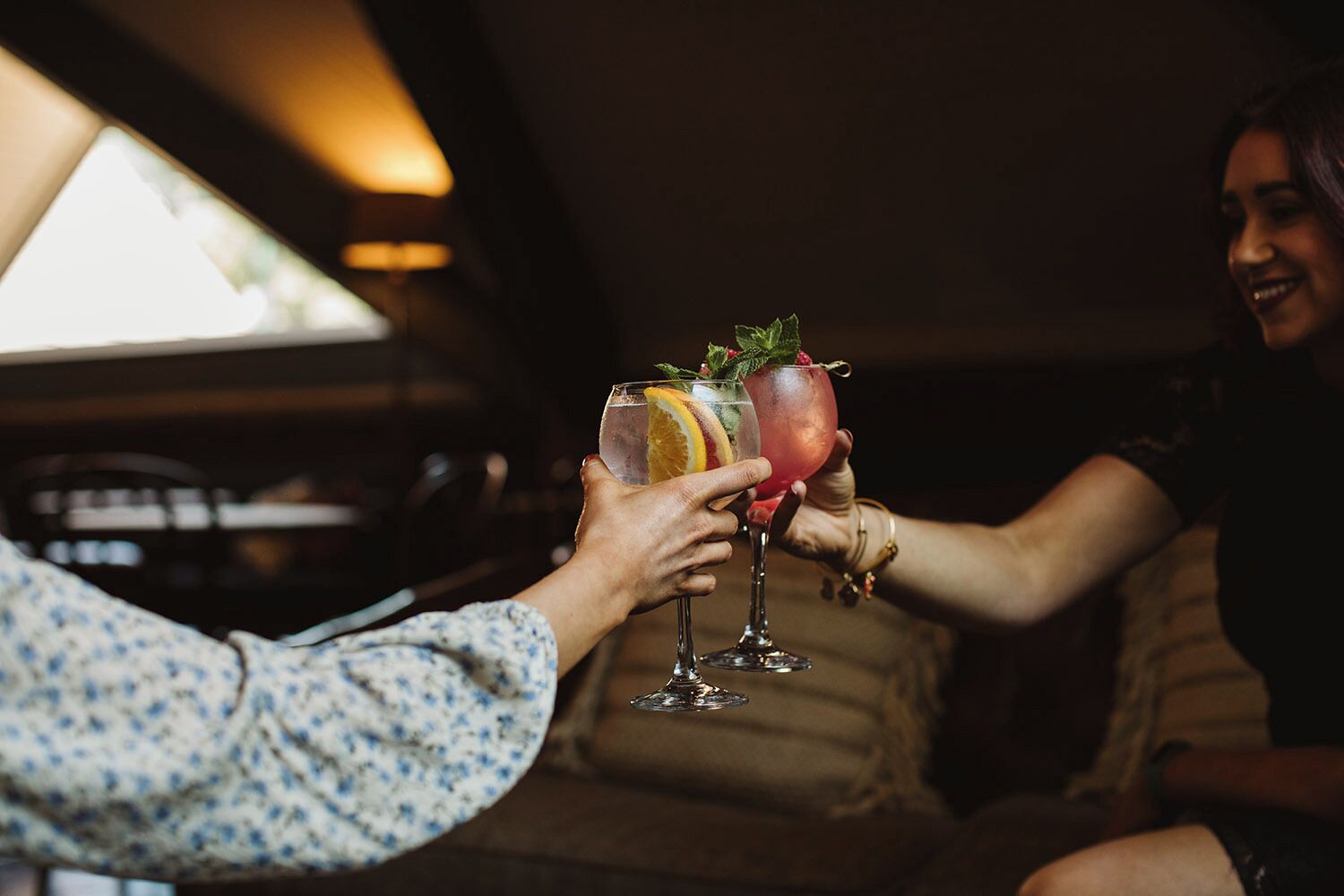 Two people toasting with drinks in a dimly lit room.