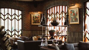 Un intérieur chaleureux avec des murs en briques, un plafond en bois et un coin salon avec des canapés et une table basse. Des œuvres d’art encadrées ornent les murs, et une plante en pot est posée sur une étagère.