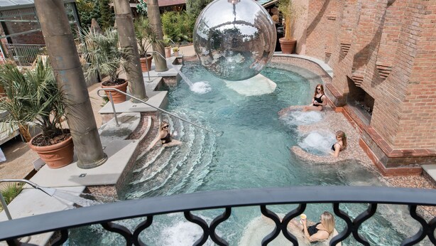 Un espace piscine agrémenté d’une grande sphère réfléchissante, d’un bâtiment en briques et de plantes en pot.