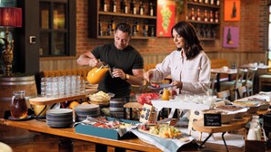 A breakfast buffet with various food items and beverages, a wine rack in the background, and a brick wall.
