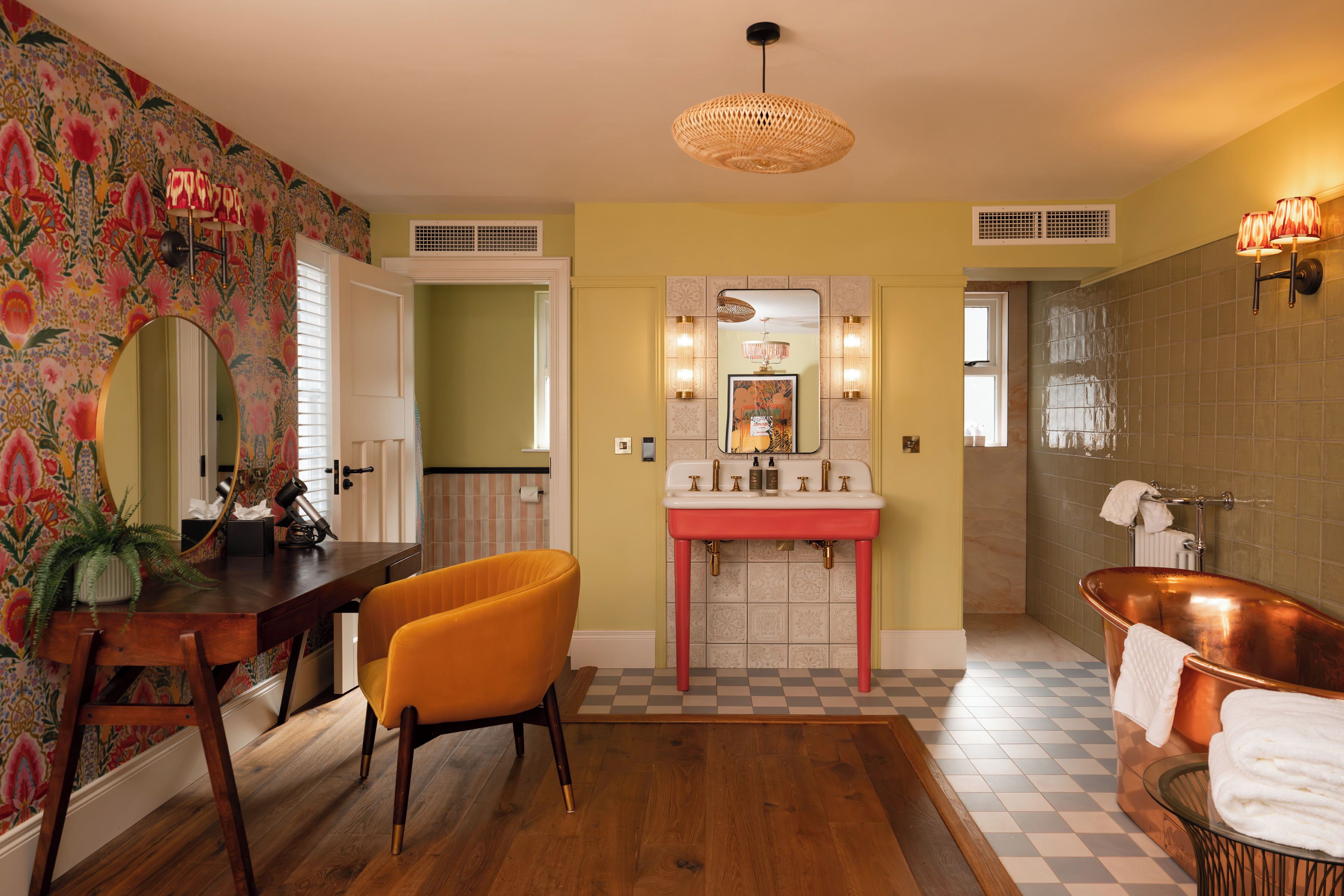 A bathroom with a checkered floor, a copper bathtub, a sink with a mirror above it, and a chair.