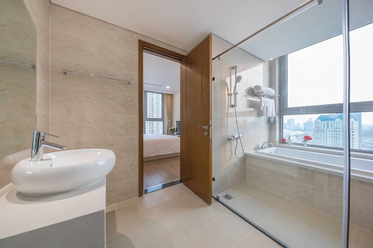 A modern bathroom with a large sink, glass shower enclosure, and a bathtub with a view of the city.