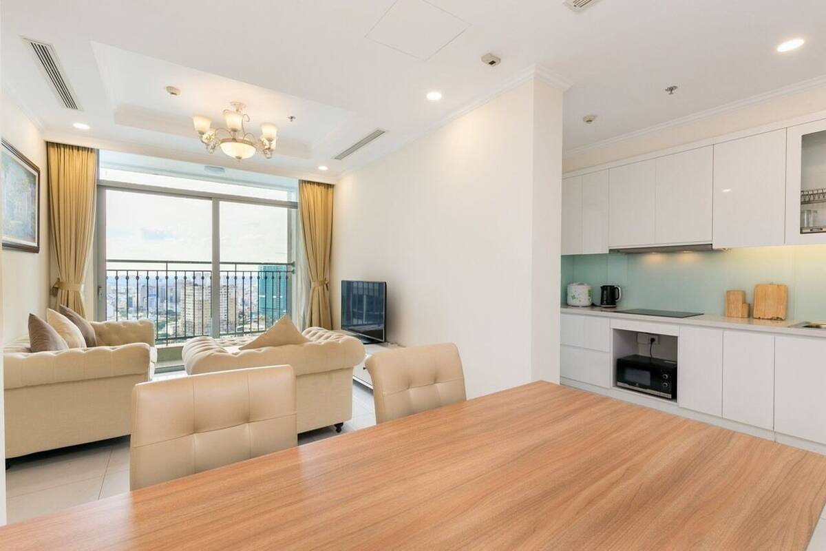 A modern living room with a large wooden dining table, beige sofas, and a TV.