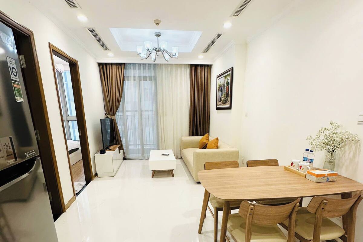 A modern hotel room with a dining area, a sofa, a TV, and a large window with curtains.