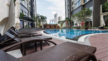 A swimming pool with lounge chairs and umbrellas, surrounded by tall buildings and greenery.