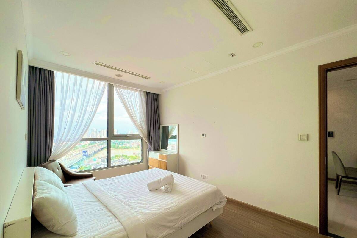 A hotel room with a bed, a window with curtains, a small desk, and a chair.