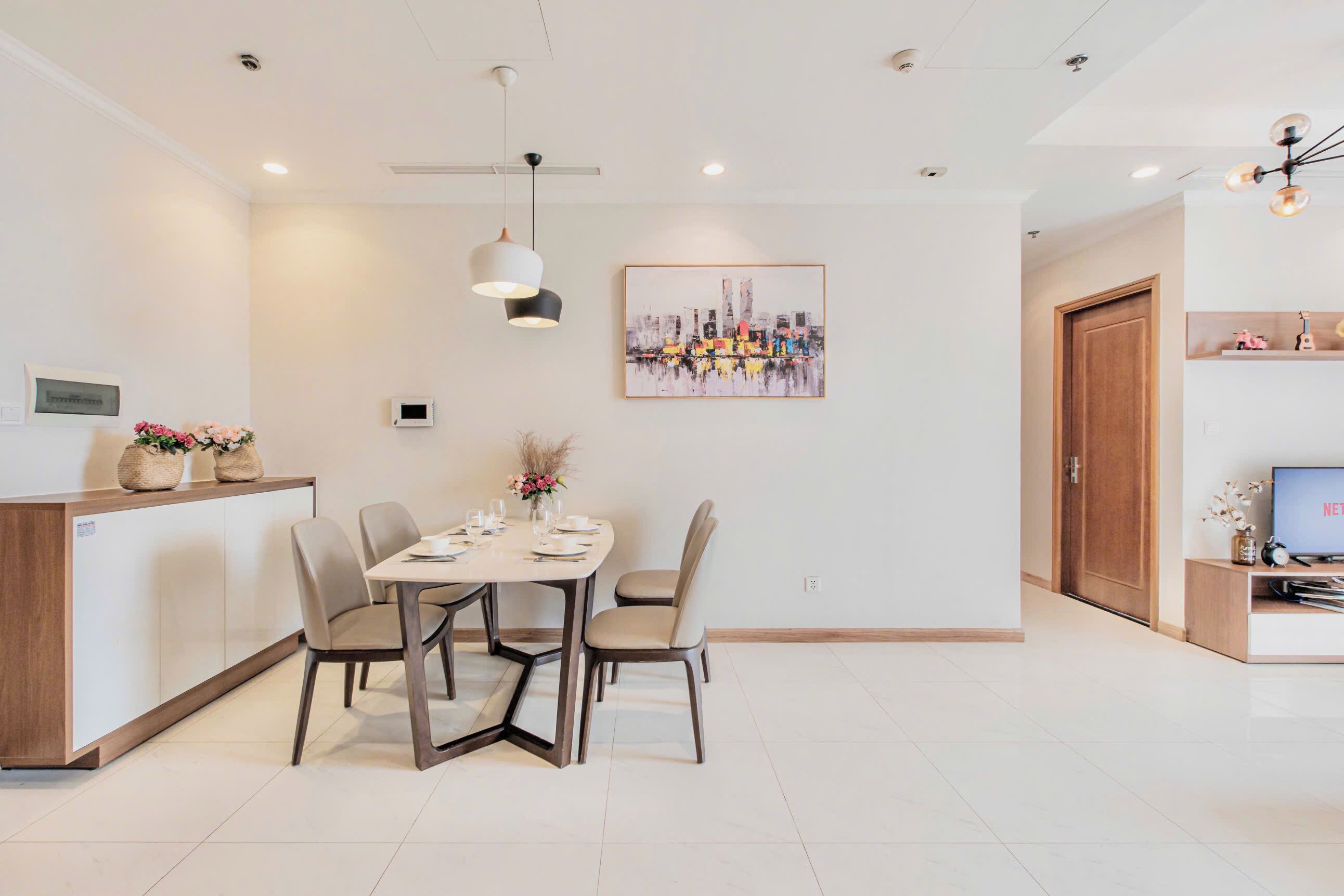 A modern dining area with a table set for four, a ceiling fan, and a framed artwork on the wall.