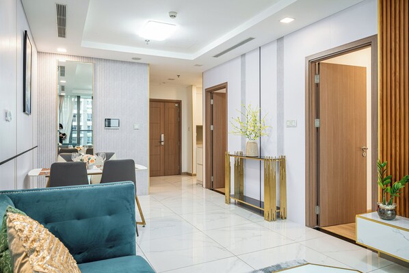 A modern living room with a teal sofa, a dining area with a table set for four, and a hallway leading to a wooden door. - Vinhomes Central Park- Luxury Apartments (Ho Chi Minh City)