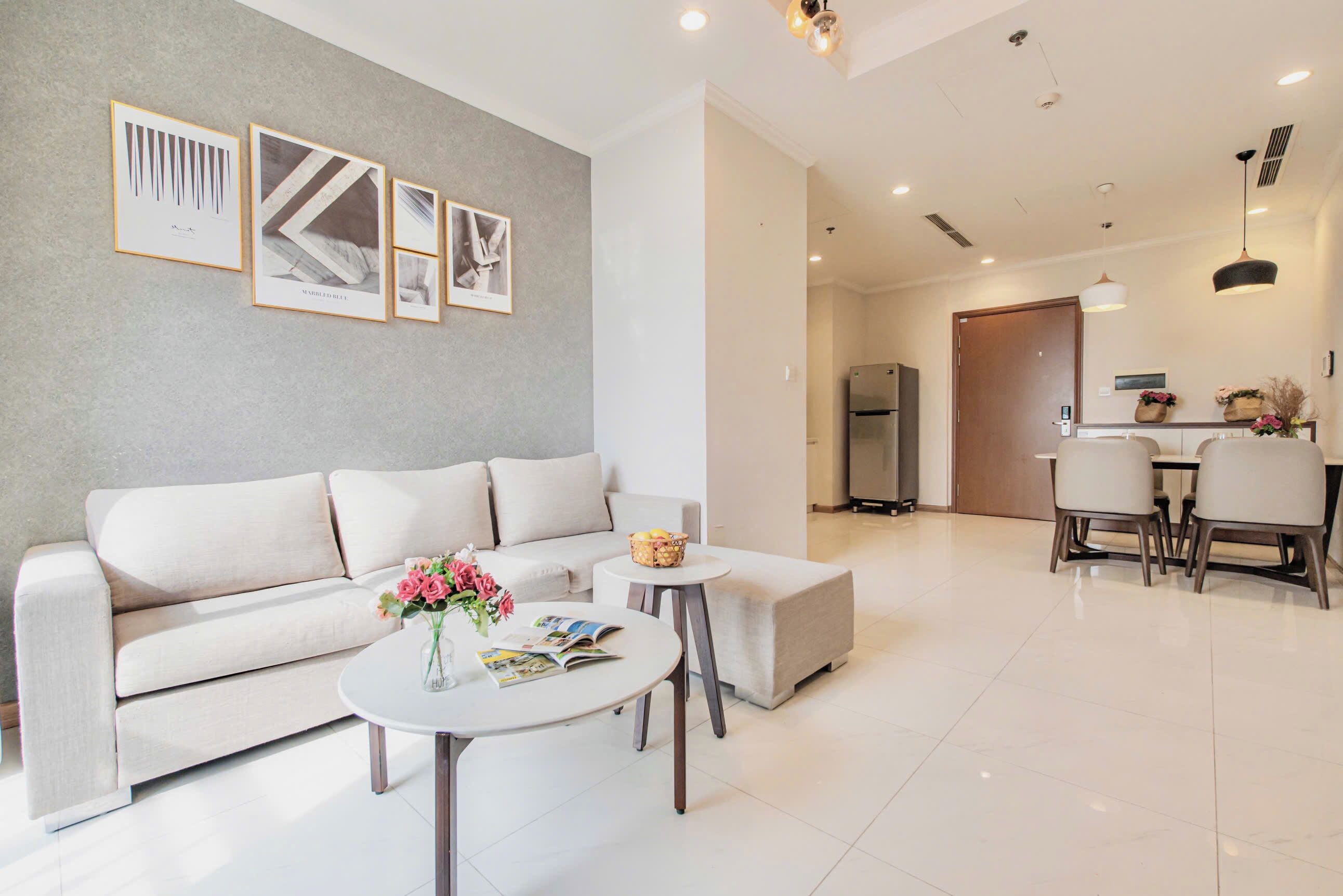 A modern living room with a sofa, a coffee table with flowers, and framed pictures on the wall.